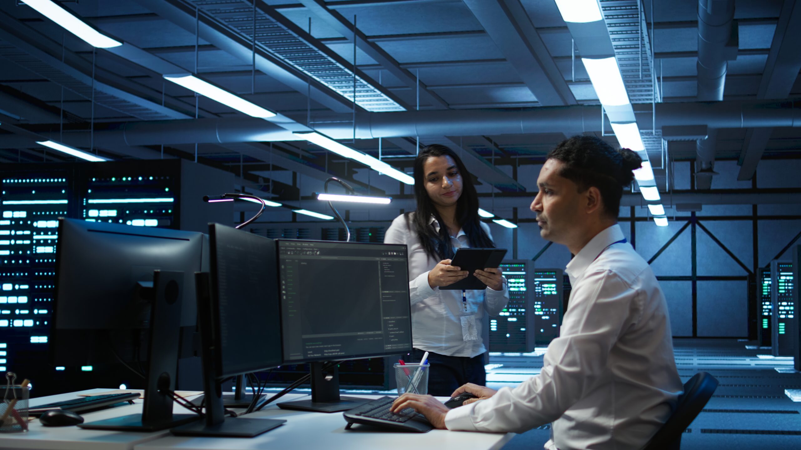 Team of programmers in high tech data center troubleshooting issues using tablet. Teamworking colleagues in server farm using device, establishing performance benchmarks, camera B